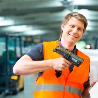 Logistics - Warehouseman with protective vest and scanner, scans bar-code of package, he standing at warehouse of freight forwarding company