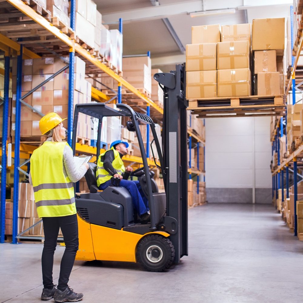 Young workers working together. Man forklift driver and a woman in a warehouse.